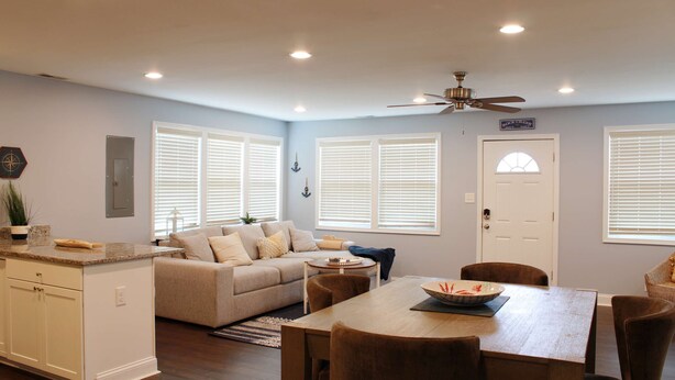 A well-lit living room with a sofa, dining table, and chairs, a kitchen area with cabinets, and a ceiling fan. - Pet Friendly Water View Cottage (Pasadena)