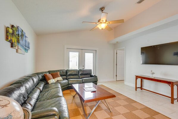 A living room with a sectional sofa, a coffee table, a ceiling fan, and a flat-screen TV on the wall. - 1 Mi to Beach: Family-Friendly Home in PCB! (Panama City Beach)
