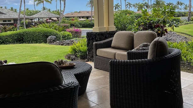A covered outdoor seating area with wicker furniture, a view of the ocean, and palm trees. - Kolea 10D: 3 Bed/3 Bath Garden Level Condo w Direct Access to Pool & Ocean. (Waikoloa Village)