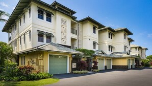 A multi-story residential building with a symmetrical facade, multiple garage doors, and a well-maintained lawn. - Kolea 10D: 3 Bed/3 Bath Garden Level Condo w Direct Access to Pool & Ocean. (Waikoloa Village)