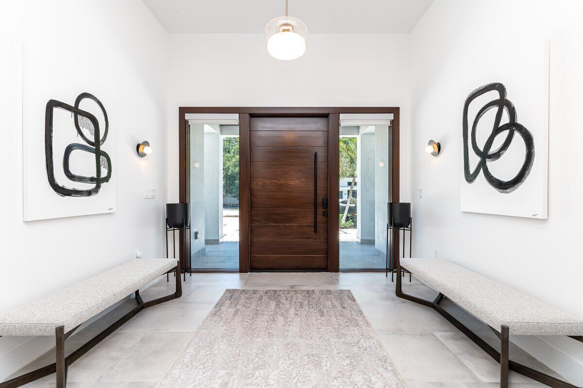 Un intérieur moderne avec une porte en bois, deux bancs, des œuvres d’art abstraites accrochées au mur et un luminaire.