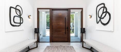 Un intérieur moderne avec une porte en bois, deux bancs, des œuvres d’art abstraites accrochées au mur et un luminaire.