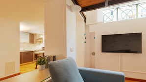 A living room with a grey sofa, a TV mounted on the wall, and a kitchen in the background. - GuestHost - Cozy apartment in St. Ambrose! (Milano)