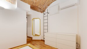 A room with a wooden floor, white walls, a white bed, a mirror with a gold frame, a white wardrobe, and a radiator. - GuestHost - Cozy apartment in St. Ambrose! (Milano)