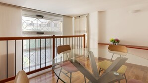 A balcony with a glass table and chairs, a wooden railing, and a view of buildings through the window. - GuestHost - Cozy apartment in St. Ambrose! (Milano)