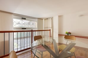 A balcony with a glass table and chairs, a wooden railing, and a view of buildings through the window. - GuestHost - Cozy apartment in St. Ambrose! (Milano)