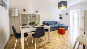 Uma sala de estar moderna com área de jantar, um sofá azul, uma mesa branca e um abajur estampado.