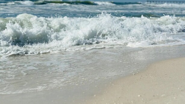 Ein Strand mit brechenden Wellen unter blauem Himmel.