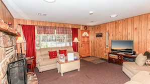 A cozy living room with a fireplace, wooden walls, a sofa, a television, and a red curtain.