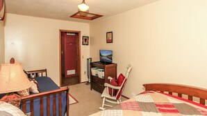 A bedroom with a bed, a chair, a desk with a computer, and a ceiling fan.