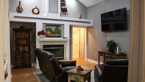 A living room with a fireplace, leather chairs, a bookshelf, and a TV mounted on the wall. - A Little Southwest in the Southeast! Great Pool Home in Jacksonville! (Jacksonville)