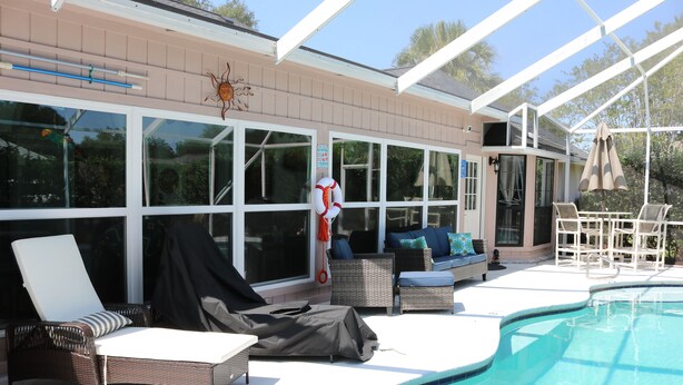 A covered outdoor area with a pool, lounge chairs, and a seating area with cushions. - A Little Southwest in the Southeast! Great Pool Home in Jacksonville! (Jacksonville)