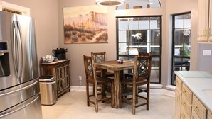 A kitchen with a stainless steel refrigerator, wooden dining table, and chairs. There is a trash can and a window with a view of the outside. - A Little Southwest in the Southeast! Great Pool Home in Jacksonville! (Jacksonville)