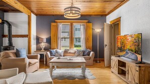 Una sala de estar acogedora con chimenea, sofá, televisor y un cuadro con una escena de bosque.