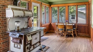 Una cocina rústica con una estufa antigua, sillas de madera y ventanas amplias.