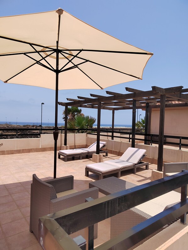 Terraza en la azotea con sillones de sol y una sombrilla grande, con vistas a la costa.