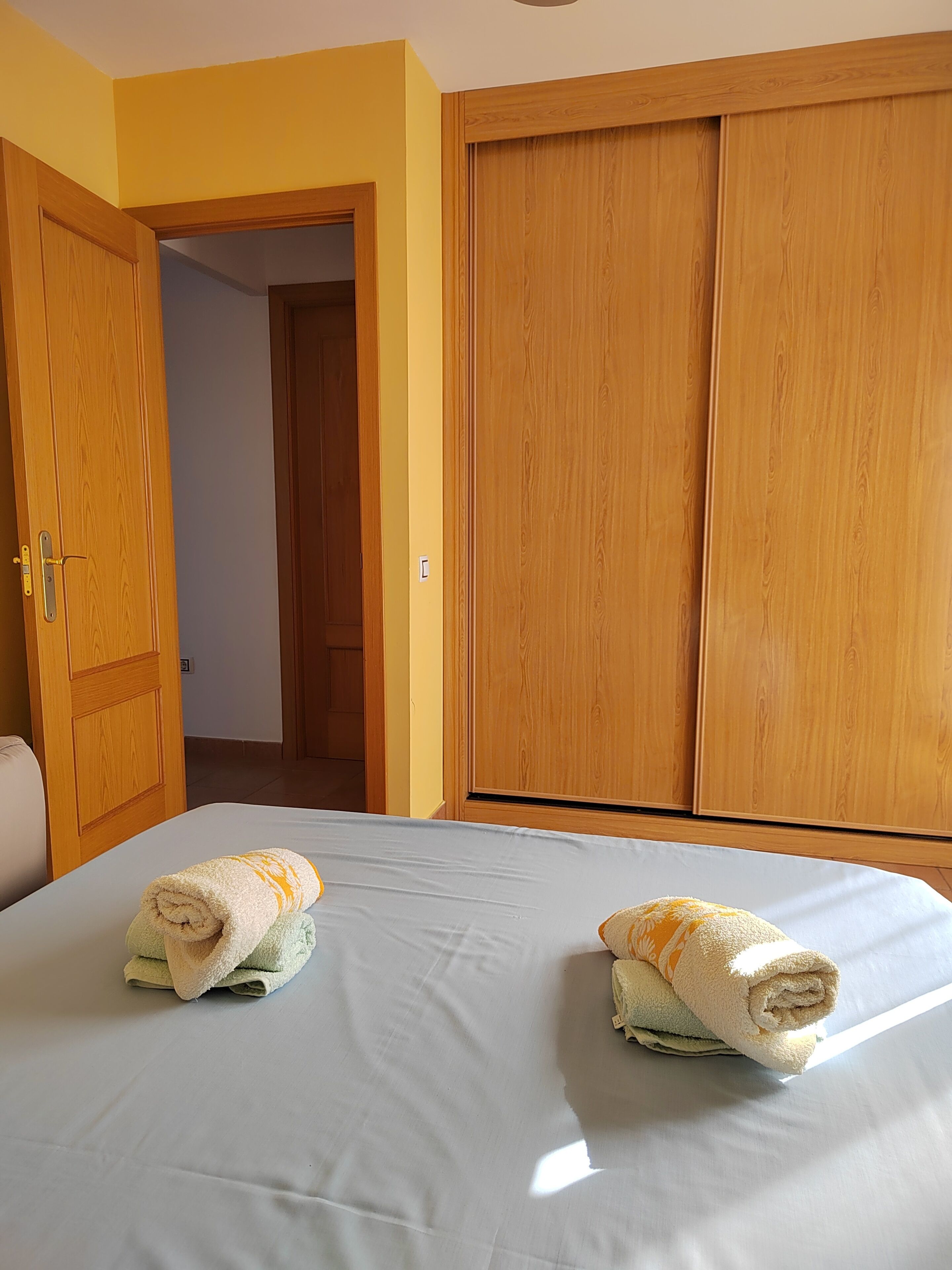 Hotellihuone, jossa on sänky, kaksi pyyhettä, puinen vaatekaappi ja ovi.