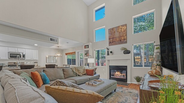 A spacious living room with a fireplace, large windows, and a modern kitchen in the background.