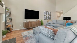 A modern living room with a grey sofa, a wooden console table, and a flat-screen TV mounted on the wall.