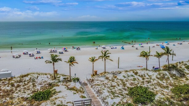 Een strand met helder turquoise water, palmbomen en strandstoelen.