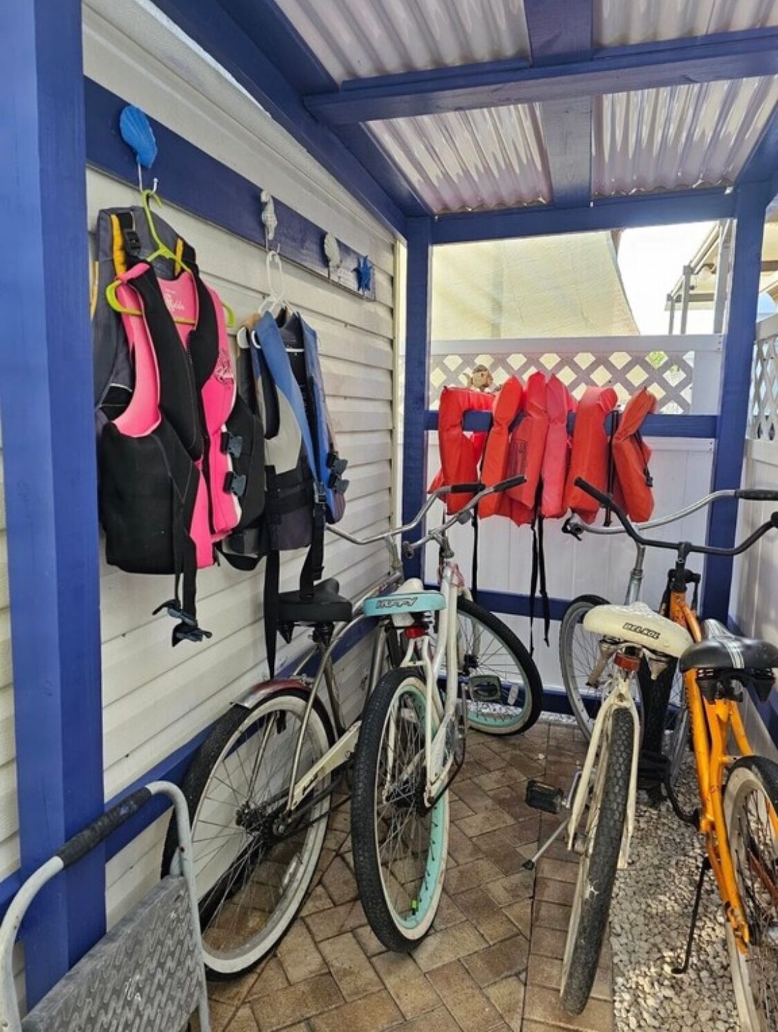 A covered bicycle parking area with a white wall and blue trim. There are two bicycles parked, one with a white frame and the other with an orange frame.
