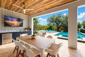 An outdoor dining area with a pool and lounge chairs, a ceiling fan, and a view of the pool.