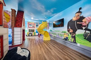 A children's play area with a slide, a playhouse, and a mural with animated characters.