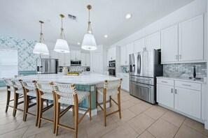 A modern kitchen with white cabinetry, stainless steel appliances, and a central island with bar stools. - Reunion 10BR Villa with Private Pool & Theater (Kissimmee)