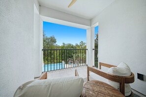A balcony with a wooden bench and a white cushion, overlooking a swimming pool and greenery. - Reunion 10BR Villa with Private Pool & Theater (Kissimmee)