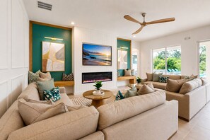 A living room with a fireplace, a ceiling fan, and a large window with a view of greenery.