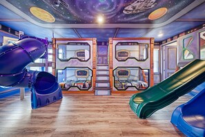A room with bunk beds, slides, and a space-themed ceiling.