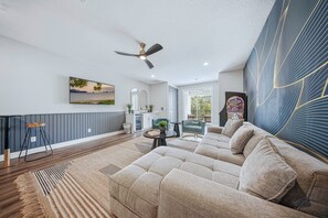 A modern living room with a sectional sofa, a ceiling fan, a dining area with a table and chairs, and a large window with a view. - Reunion 10BR Villa with Private Pool & Theater (Kissimmee)