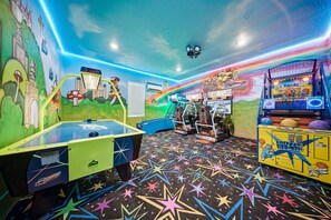 A colorful arcade room with various gaming machines, including a racing game and a basketball game. - Glamorous Getaway With Themed Bedrooms at Reunion (Kissimmee)