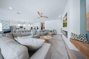 Ein modernes Wohnzimmer mit einem großzügigen Ecksofa, einem Couchtisch und einem Essbereich, im Hintergrund ist eine Küche erkennbar.