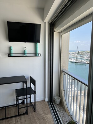 A balcony with a view of a marina, a flat-screen TV mounted on the wall, and a small table with a chair.