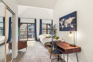 Une chambre d’hôtel avec un lit, un bureau et une chaise, une carte accrochée au mur et une vue sur le balcon extérieur.
