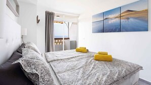 Una habitació d'hotel amb un llit, una finestra amb cortines, un ventilador de sostre i una obra d'art penjada a la paret.
