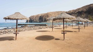 Una platja amb paraigües de palla i un llinatge rocos.
