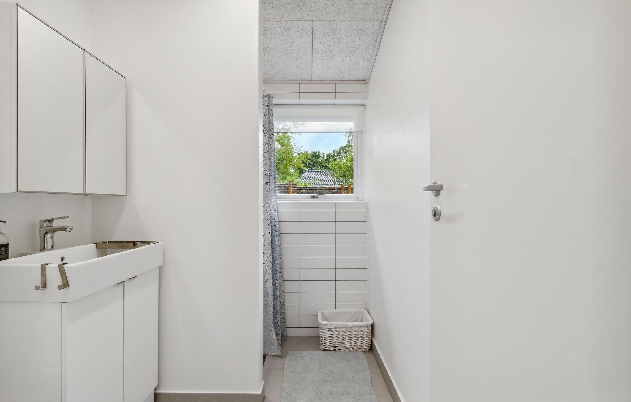 A narrow bathroom with a window, a sink, and a shower area.