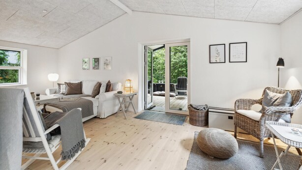 A cozy, well-lit room with a sofa, a dining table, and a wicker chair. A sliding glass door leads to an outdoor area with a garden view. - 3 bedroom pet friendly home in Græsted (Græsted)