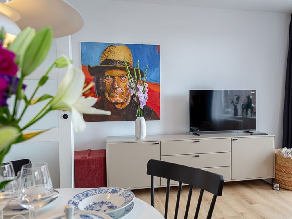 A modern living room with a dining area, a flat-screen TV, and a painting on the wall.