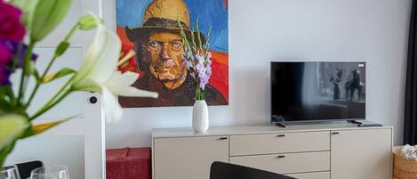 A modern living room with a dining area, a flat-screen TV, and a painting on the wall.