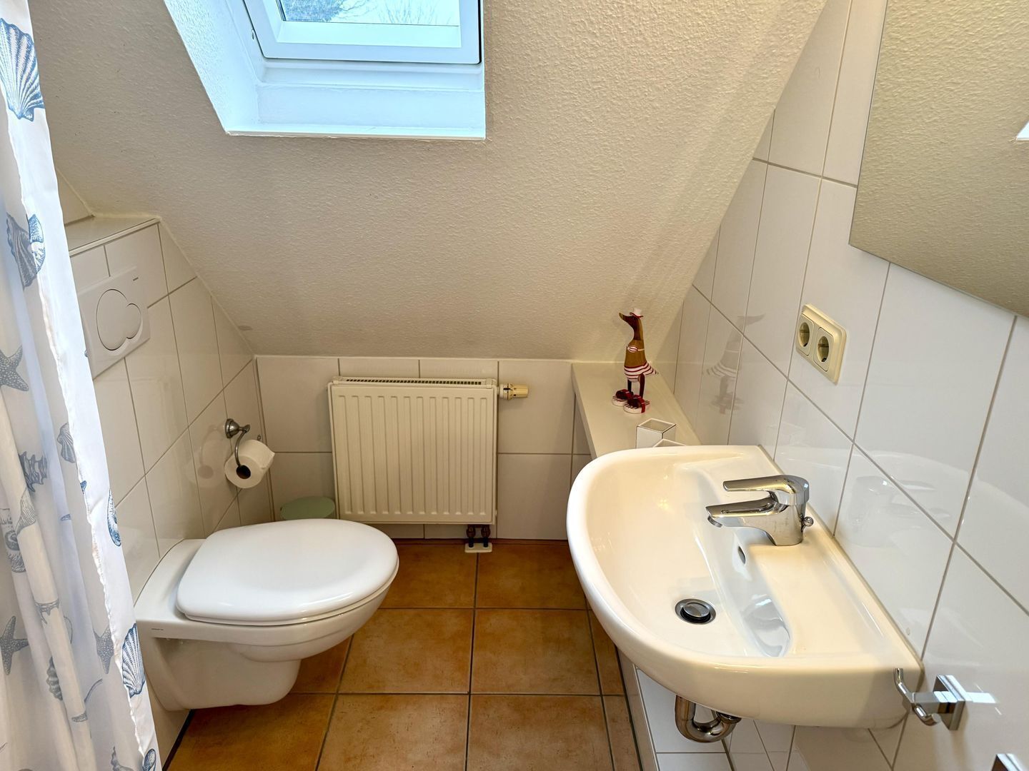 Une petite salle de bain comprenant des toilettes, un lavabo et une lucarne située au-dessus des toilettes.