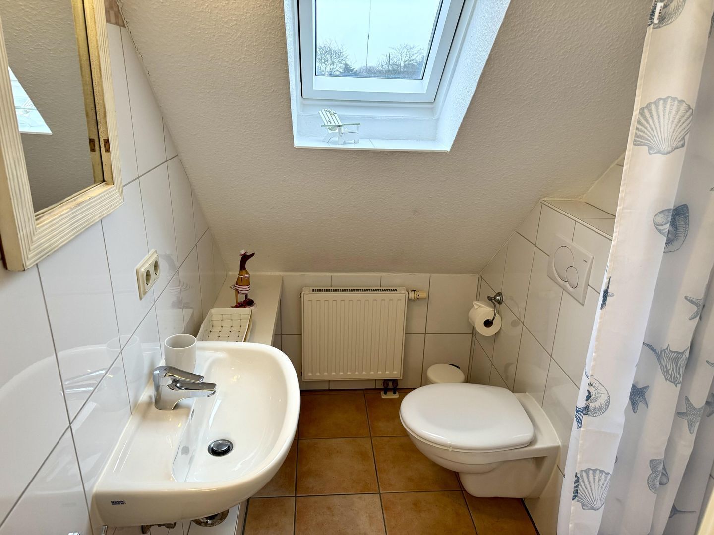 A small bathroom with a skylight, a sink, a toilet, and a shower curtain with a sea shell pattern.