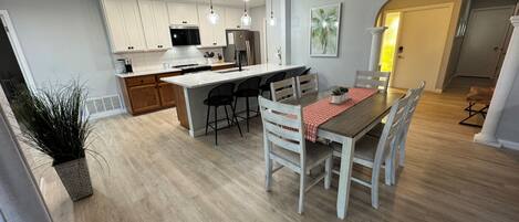 Uma cozinha moderna com armários brancos, uma ilha central e um espaço de jantar com mesa e cadeiras de madeira.