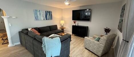 A living room with a grey sofa, a patterned armchair, a flat-screen TV, and a fireplace.