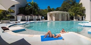 A swimming pool with lounge chairs and a sunbed, surrounded by palm trees and a building with a white facade. - Royal Suites of Lifestyle Holiday Resort - All inclusive (Puerto Plata)