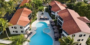 A resort with a central swimming pool, multiple buildings with red-tiled roofs, and palm trees. - Royal Suites of Lifestyle Holiday Resort - All inclusive (Puerto Plata)