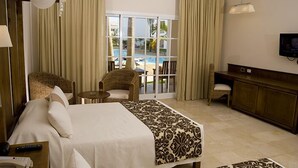A hotel room with a bed, two chairs, a small table, a TV, and a view of an outdoor swimming pool. - Royal Suites of Lifestyle Holiday Resort - All inclusive (Puerto Plata)