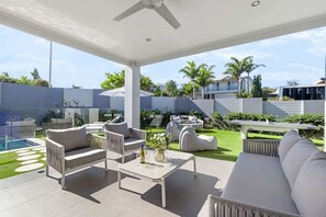 Um alpendre coberto com móveis modernos, piscina e vista para o bairro.